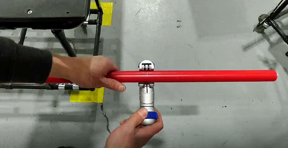 Hands using a manual pipe cutter to make a clean, straight cut on a red Flexpipe tube.