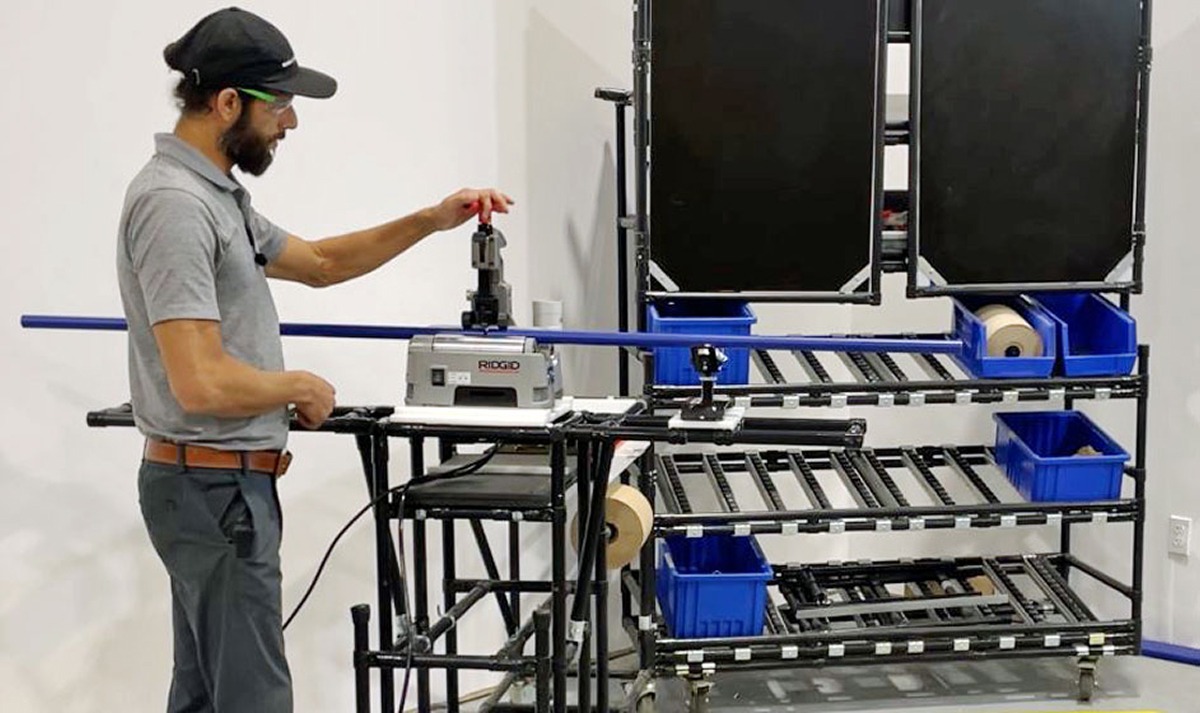 Technician operating a power tubing cutter to cut a Flexpipe tube at an assembly station.