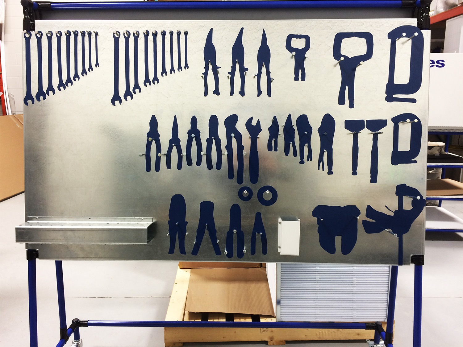 5S tool shadow board with tool silhouettes on a metal board for electrical equipment assembly and maintenance.