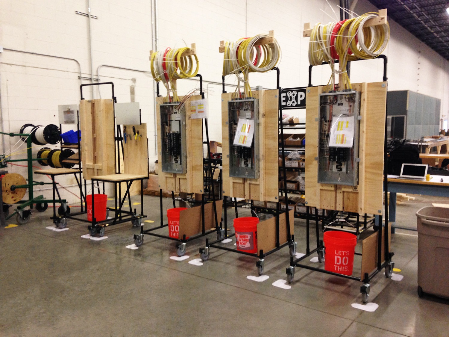 Mobile workstations with wooden panel boards, electrical boxes, and wire spools for electrical panel assembly