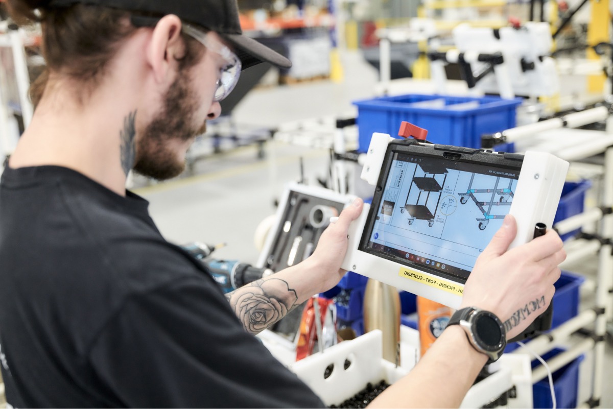 A manufacturing worker using a digital tablet to follow assembly instructions for a modular cart in an industrial environment.