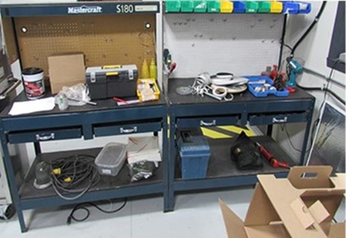 two welded workstations side-by-side. Each workstation has one work level and two pull out drawers. This workstation is poorly organized with multiple materials and tools spread randomly on the work surface. There are multiple tripping hazards and potential dangers. It is not a 5S workstation and is not lean.