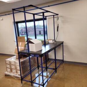 Modular blue pipe workstation with overhead frame for hanging tools in an electrical equipment assembly workspace.