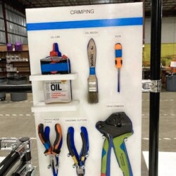 Shadow board for crimping tools with organized compartments for oil cans, brushes, and pliers in a 5S industrial workspace