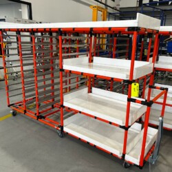 Modular red pipe kitting cart with white plastic trays and casters, designed for efficient material handling in an industrial assembly or logistics environment.