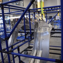 Heavy-duty blue pipe automotive rack used for storing and transporting large stamped metal parts in a manufacturing warehouse.